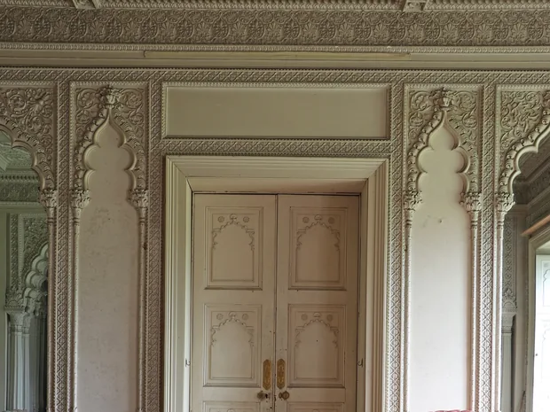 An interior doorway at Elveden framed by carved foliate plaster panels and cusped niches, the doors themselves panelled with arched motifs