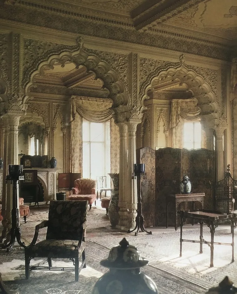 A drawing room at Elveden: deeply carved cusped arches and columns around the windows and chimneypiece, hung with European furniture, screens and lamp standards