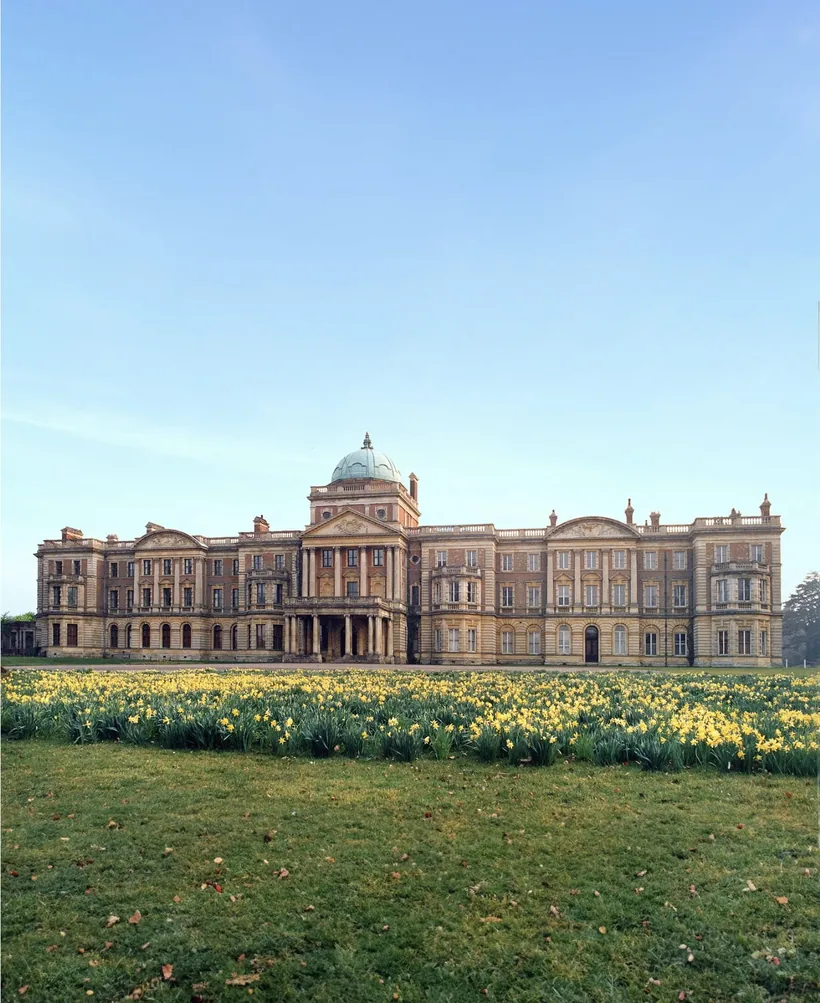 Elveden Hall from the park: a long Italianate country house in brick and stone with a green copper dome over the centre, daffodils in the foreground